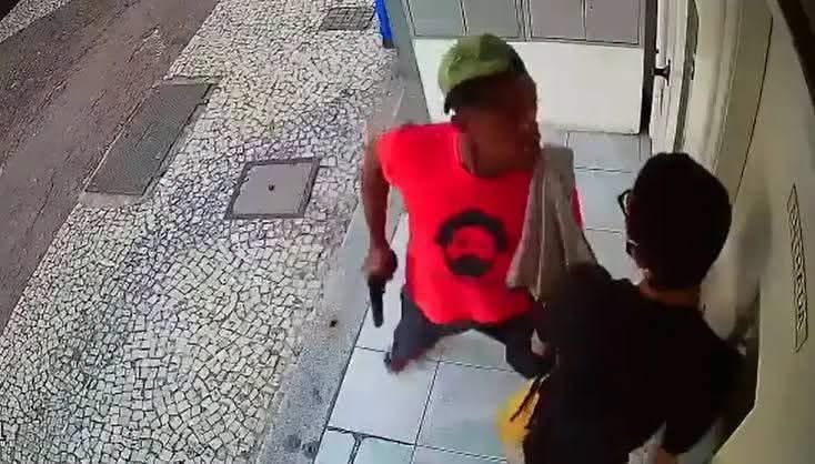 Print de câmera de segurança: homem aponta arma contra vítima usando camiseta vermelha com o rosto de Lula.