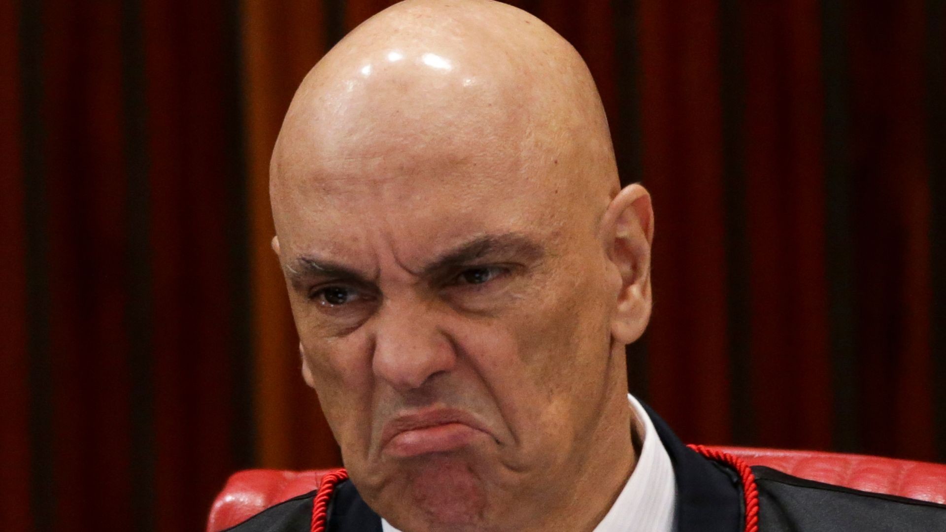 Close do rosto de Alexandre de Moraes de toga, com sobrancelhas franzidas e boca em careta exagerada, formato clássico de meme de reação.